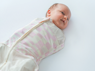 Baby swaddled in Pink Check Sleepea smiling
